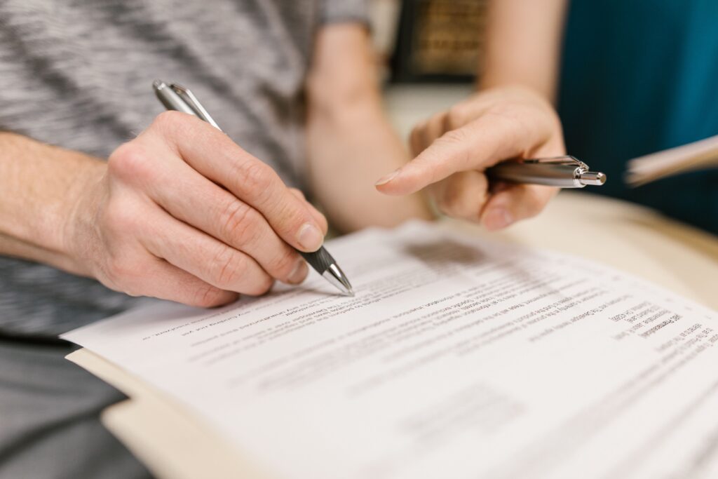 Close-up of two adults reviewing and signing a legal document with pens indoors